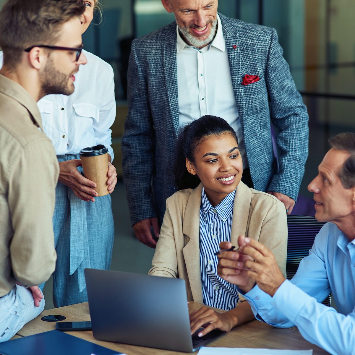 Cheerful multiracial business team using laptop, discussing project results and smiling while having a meeting in the modern office, working together. Teamwork, cooperation, collaboration